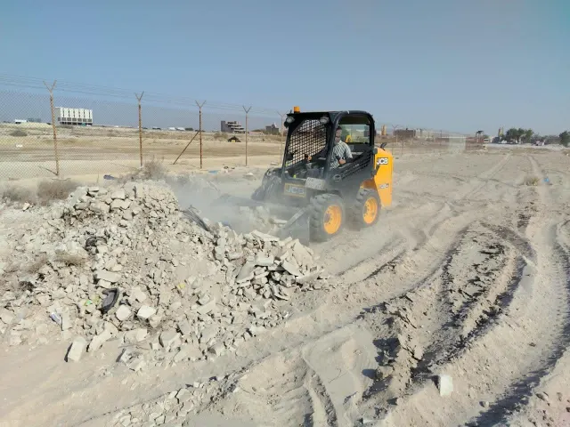 لودر صغير يجمع المخلفات والتربة الملوثة من موقع مسوّر