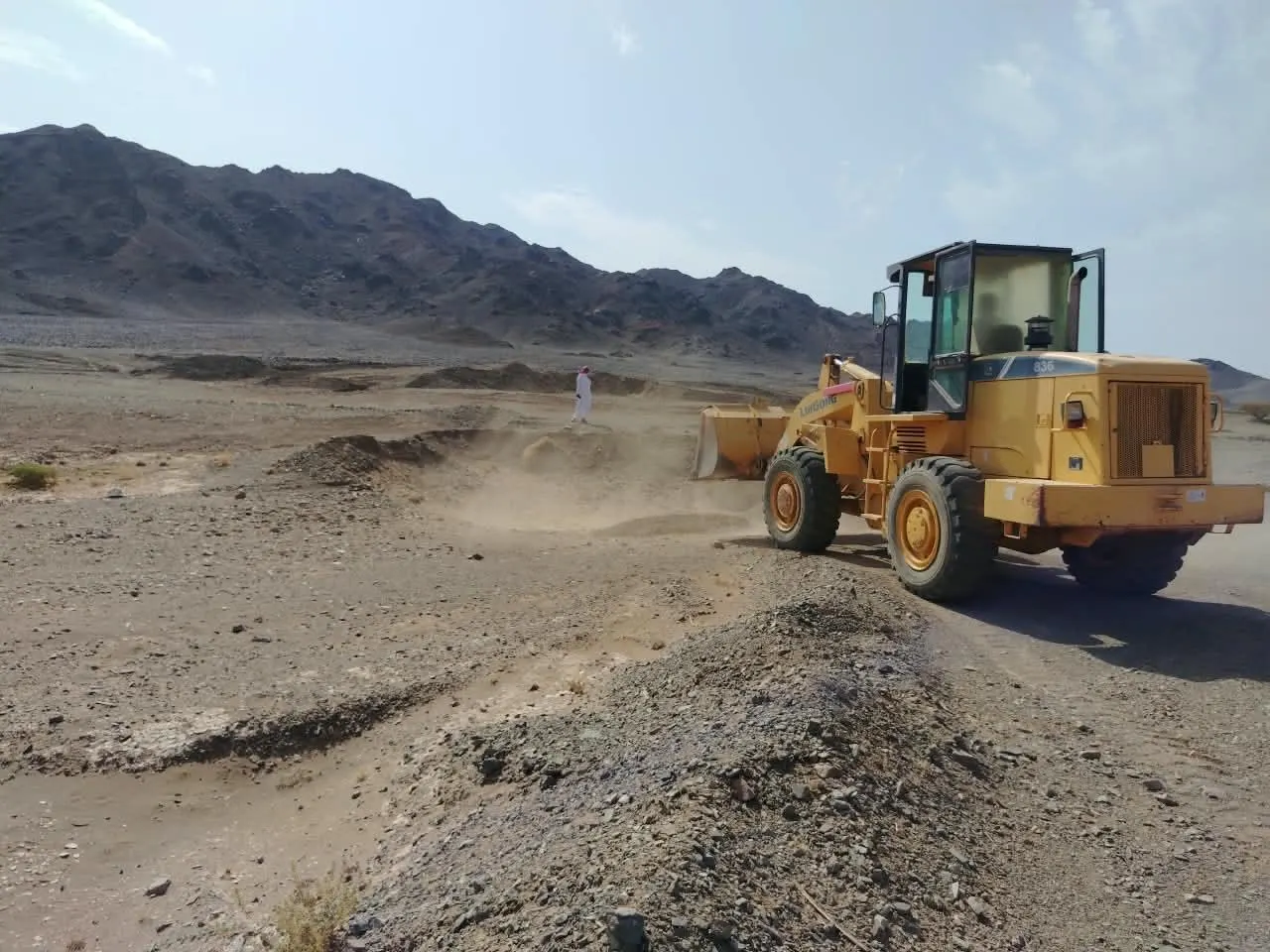 لودر يسوّي أرض موقع تعديني عند سفح الجبال