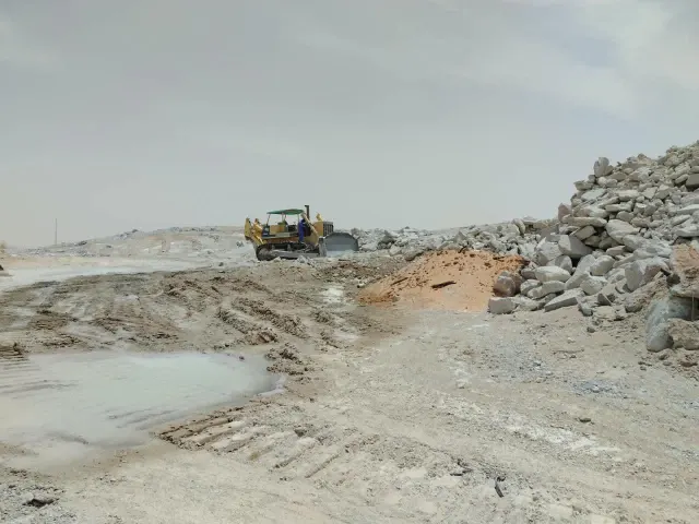 جرّافة تسوّي أرض محجر بجوار أكوام الصخور ضمن أعمال إعادة التأهيل